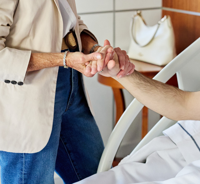 Acompañante tomando la mano de un paciente internado en una habitación del IADT.