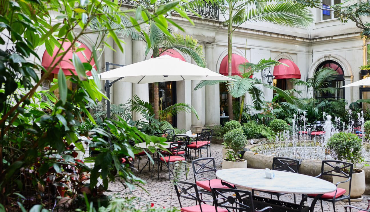 Patio interior rodeado de árboles, con una fuente central, mesas y sillas en el café del IADT